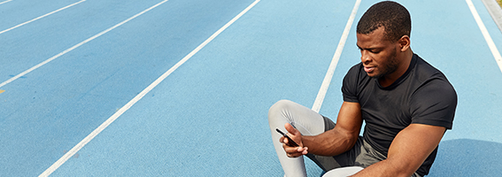 Man sitting on running track and looking at a mobile screen