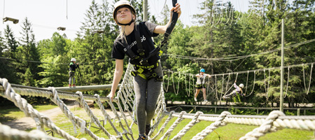 A girl in her late teens is crossing a slim rope bridge. 